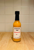 Bottle of Nomade Bangkok hot sauce on a wooden surface with a tiled wall background