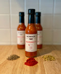 Nomade Marrakech Marrakesh hot sauce bottle on a wooden surface with middle eastern Moroccan spices in the foreground