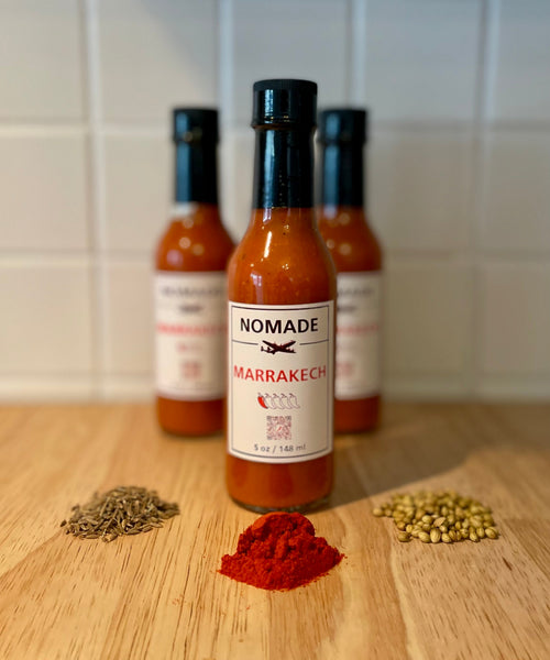 Nomade Marrakech Marrakesh hot sauce bottle on a wooden surface with middle eastern Moroccan spices in the foreground