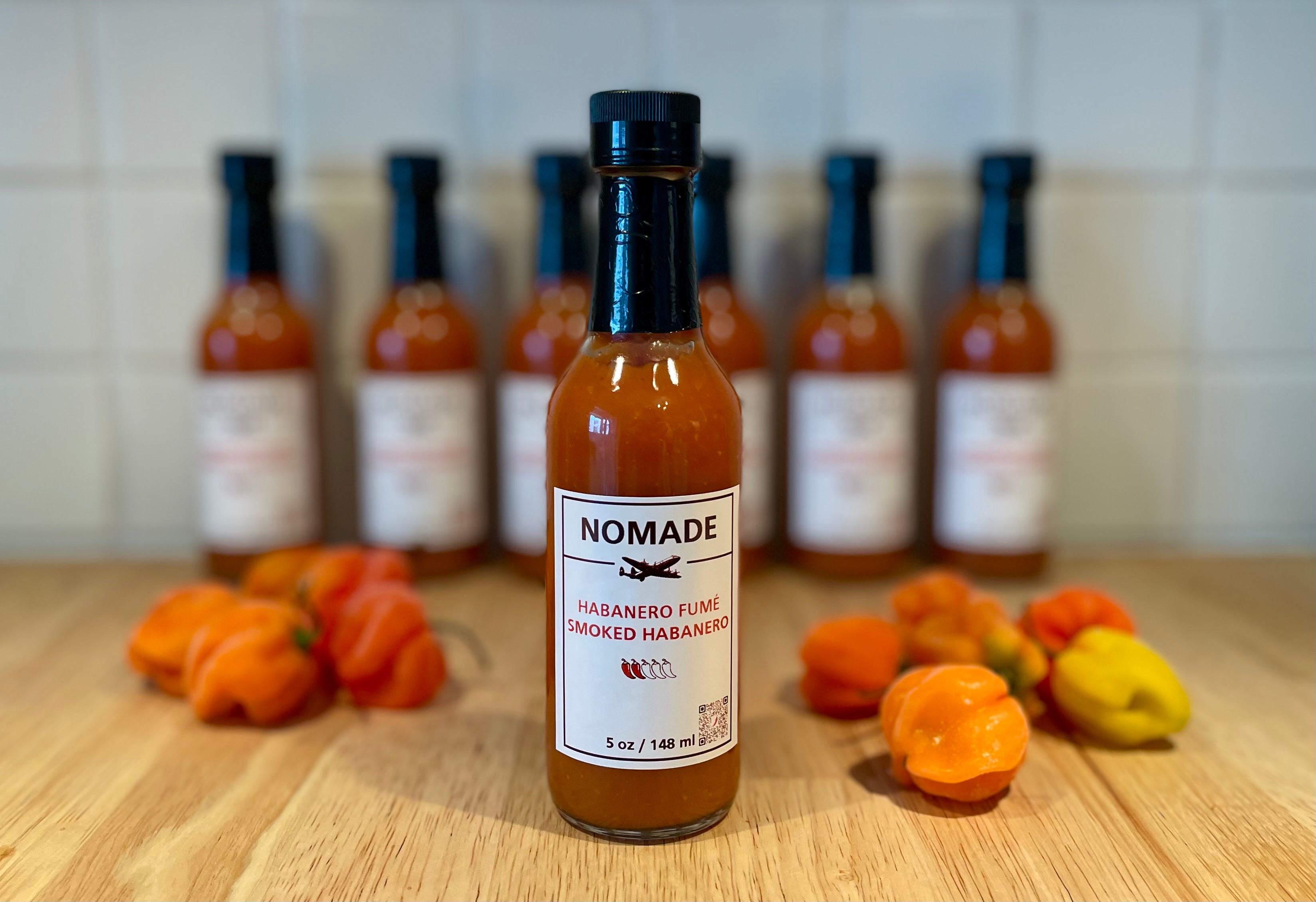 Bottle of Nomade hot sauce with habanero peppers on a wooden surface