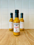 Three bottles of Nomade Waikiki sauce on a wooden surface with a white wall background.